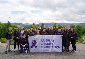 A group of Rangers Charity Foundation Staff holding a Foundation flag.