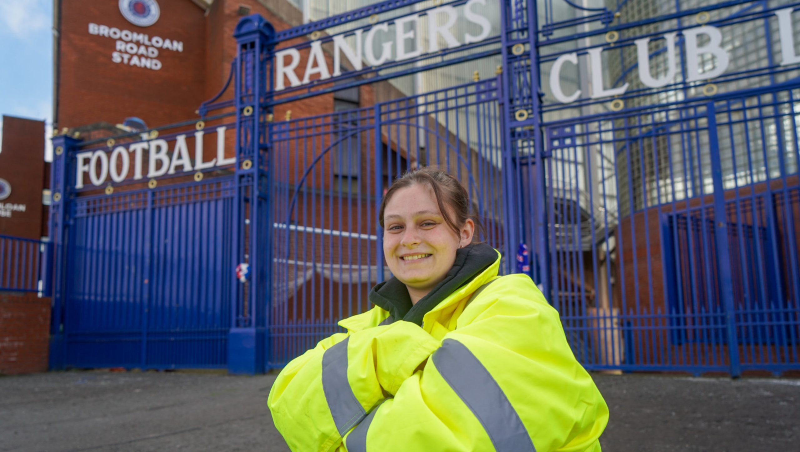 A young woman in a hi-viz jacket standing outside the Ibrox gates with her armed crossed
